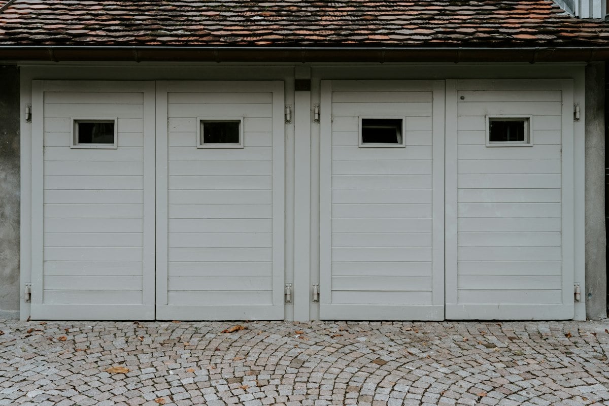 Row of white hinged garage doors with small windows