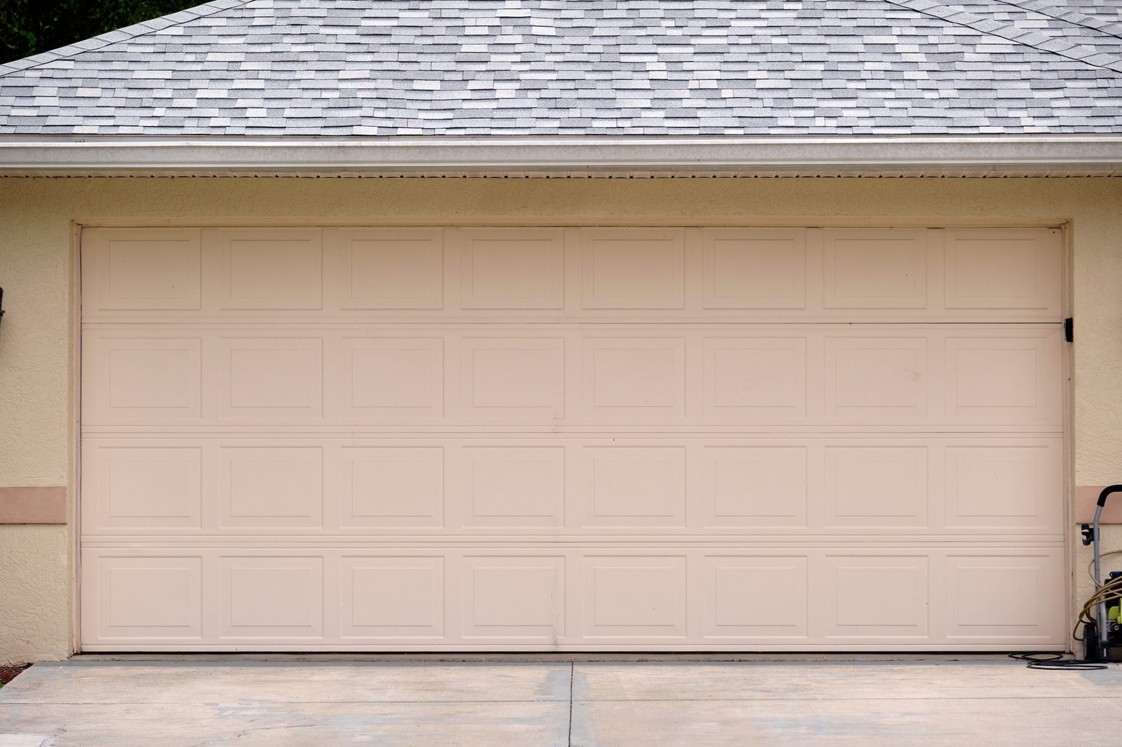 Wide beige double garage door above a concrete driveway